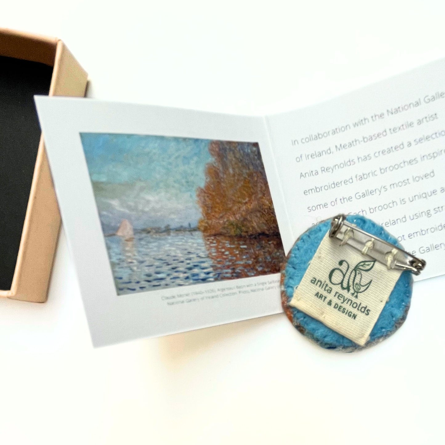 Reverse of fabric brooch with 'anita reynolds art & design' label next to its painting reproduction and box