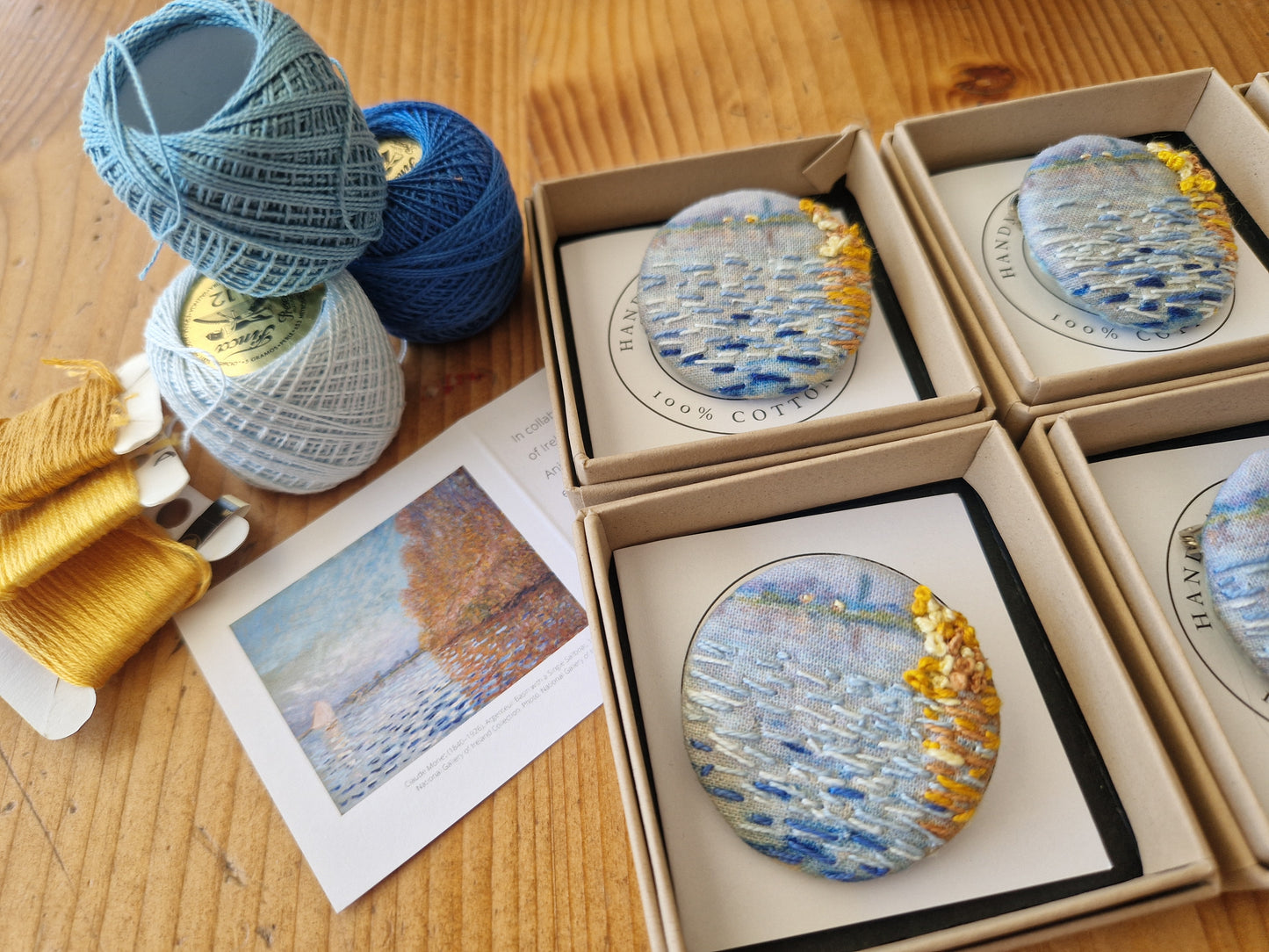 Finished Anita Reynolds brooches in their boxes alongside the threads used to embroider them