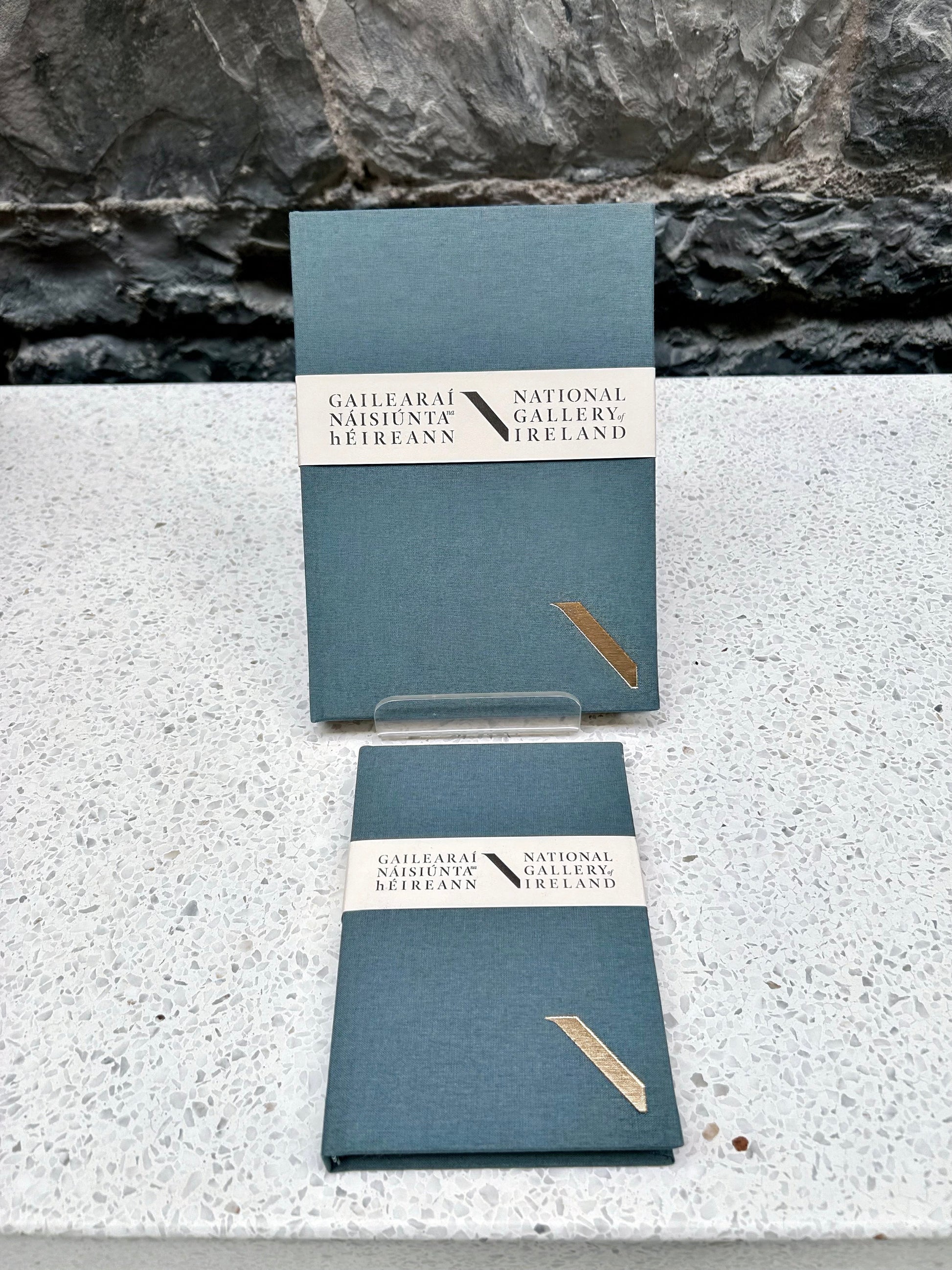 Two grey NGI and Duffy bookbinders notebooks with a National Gallery of Ireland label on a stone surface