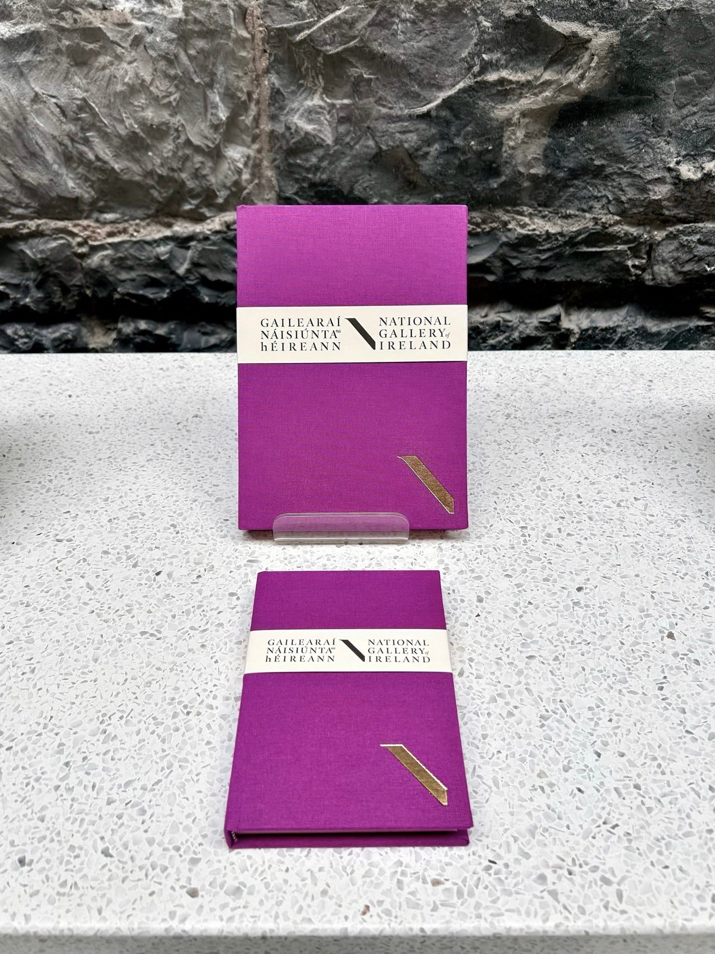 Two Purple NGI and Duffy bookbinders notebooks with a National Gallery of Ireland label on a stone surface