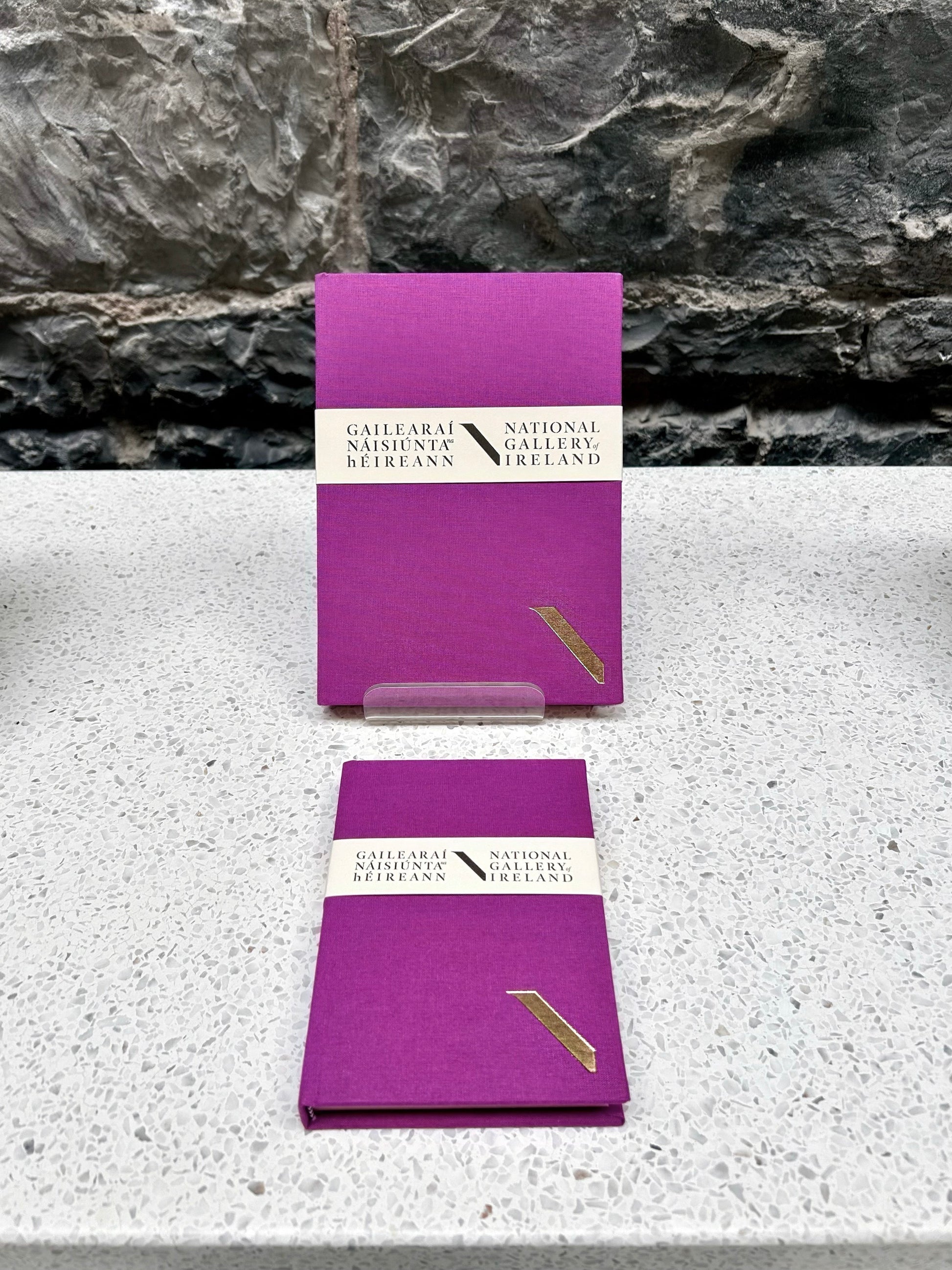 Two Purple NGI and Duffy bookbinders notebooks with a National Gallery of Ireland label on a stone surface