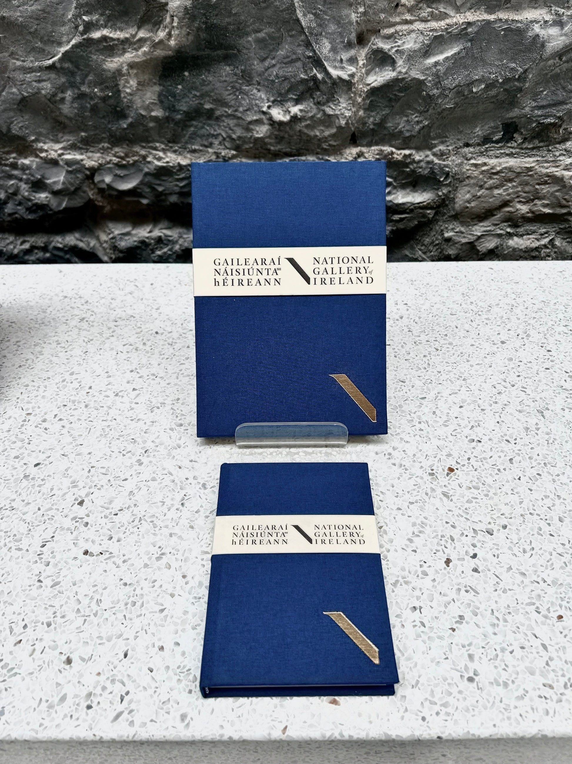 Two blue NGI and Duffy bookbinders notebooks with a National Gallery of Ireland label on a stone surface