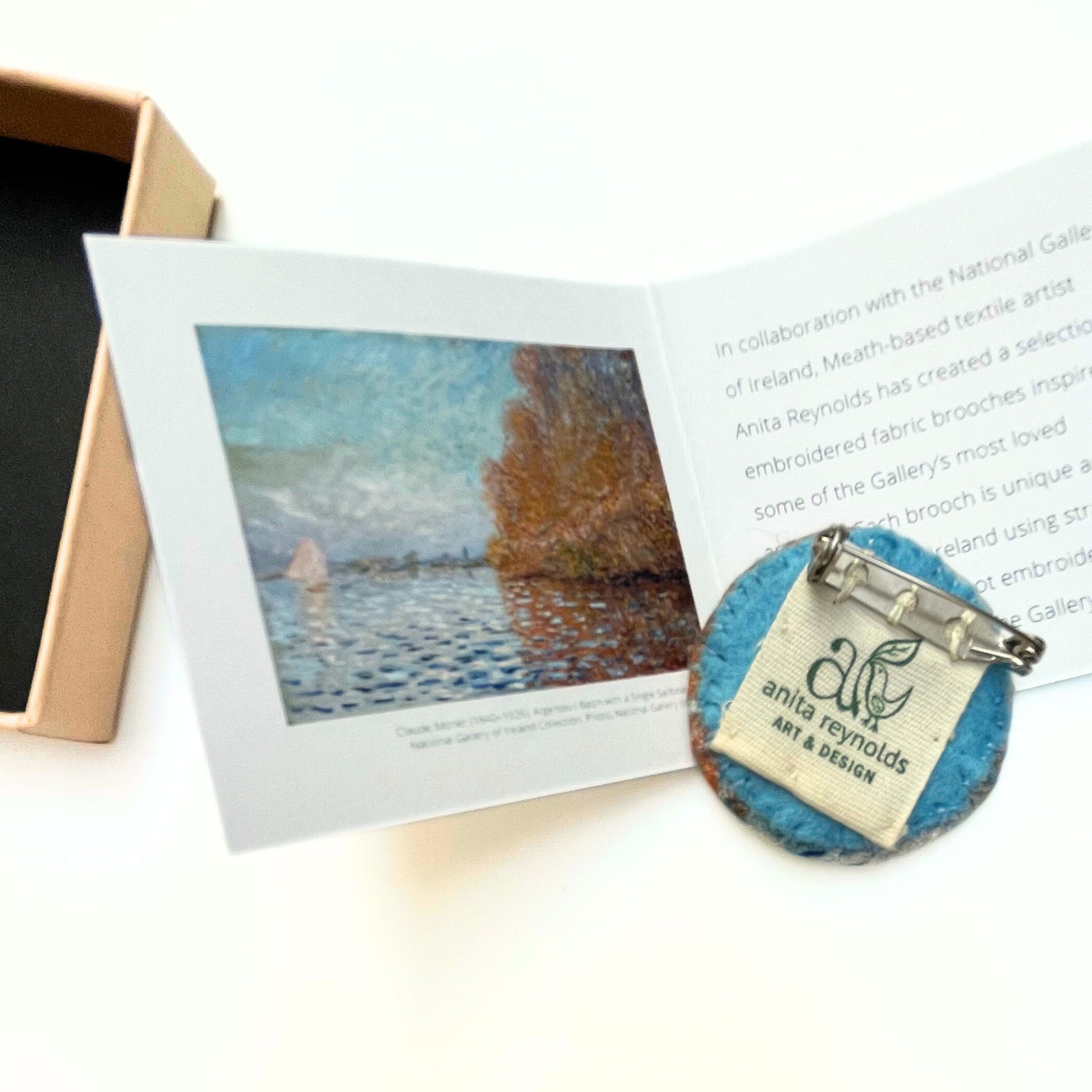 Reverse of fabric brooch with 'anita reynolds art & design' label next to its painting reproduction and box