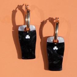A pair of black rectangular drop earrings with a silver-tone top band, a small white clover emblem, and gold hoop backings, displayed against a solid orange background.