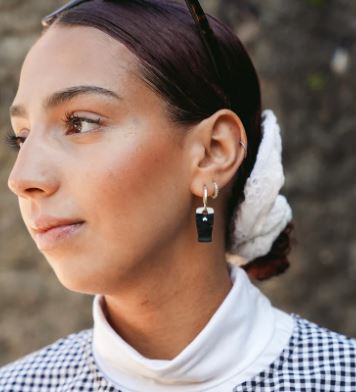 Woman with low bun wearing hoop earrings with a mini pint of stout charm. 