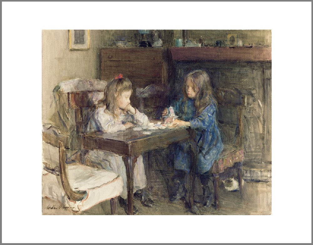 Two young girls sit at a table. Playing cards are scattered across the table and one of the girls is stacking the cards to make a house.