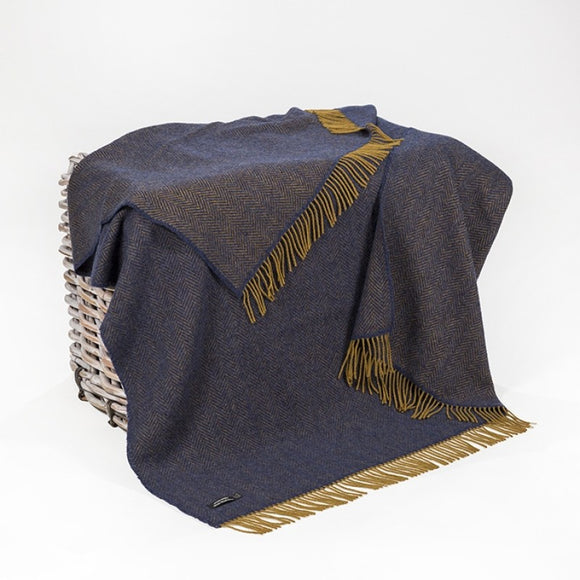 A deep navy blanket with a dark mustard fringe across the top and bottom. There is a zig-zag herringbone pattern across the blanket.