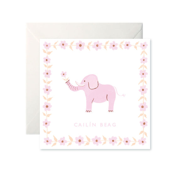 A white card with a drawing of a pink elephant holding a flower in its trunk. ‘Cailín Beag’ is written in capital letters in pink underneath. The border of the card is the same pink flower the elephant holds.