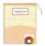 A sheer cream bag with a red drawstring. A sticker at the top has the branding and product details, and a sticker at the bottom has the towel name and a colour wheel. The towel is visible through the bag.