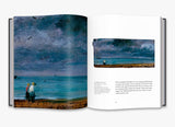 A two page spread from inside the book. The right page has a painting of a dark sky over the sea with a small couple to the left. There is explanatory text underneath. The left page is a close up of the couple and showing the texture of the sky.