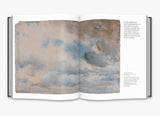 A two page spread from inside the book of a painting of a cloudy sky.
