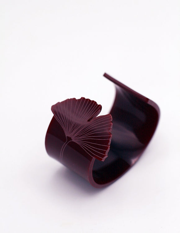 A burgundy cuff that is partially opened. One end is shaped like a ginkgo leaf with the designed etched into the bracelet.