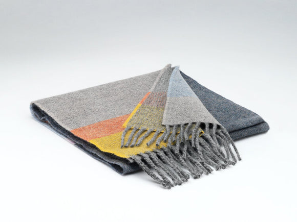 A dark grey scarf with a thick light grey, orange, and yellow stripe on the end, with grey fringe in both ends.