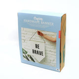 A card box with a blue bellyband. A photo of a white banner with BE BRAVE is on the band with the product details.