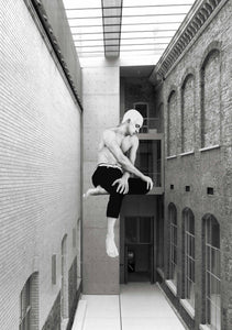 A black and white photo of a large, walled in courtyard between buildings with a glass roof. On the wall facing the viewer is an illustration of a shirtless man, legs crossed looking off to the side. It looks as if he is sitting on the wall.