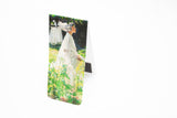An open bookmark standing upright. The front is a woman in white walking through a garden with long stemmed white lilies in the foreground.