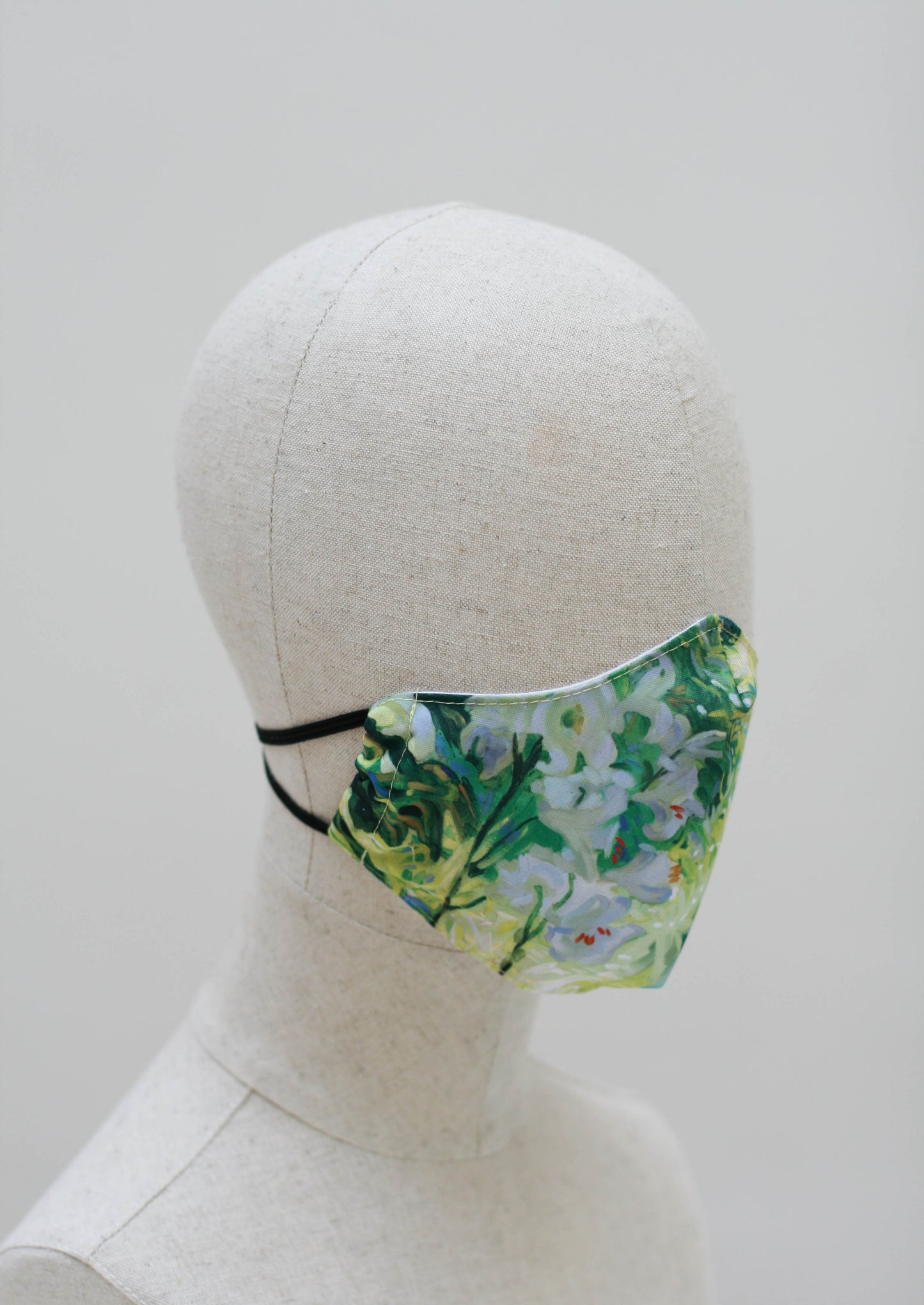 The mask on a mannequin head from the other side, showing more flowers with darker green leaves as the plants are in the shade.
