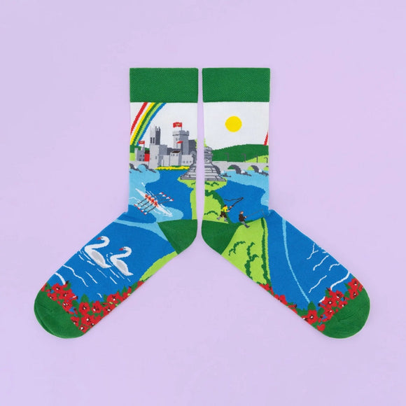 A sock with a castle, bridge, and rainbow around the leg, and a river with rowers, swans and red flowers around the foot.