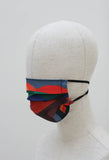 A pleated face mask is on a mannequin head. The design is a mix of abstract shapes in different colours. It has black ear straps.
