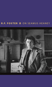 A dark blue cover with a black and white photo across the middle. A man (Heaney) stands in a kitchen holding a cup and saucer. The title is above in thin, yellow letters.