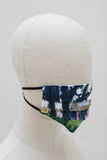The mask on a mannequin head from the other side. The landscape continues around into shade with the dark silhouette of a tree dominating the side of the mask.