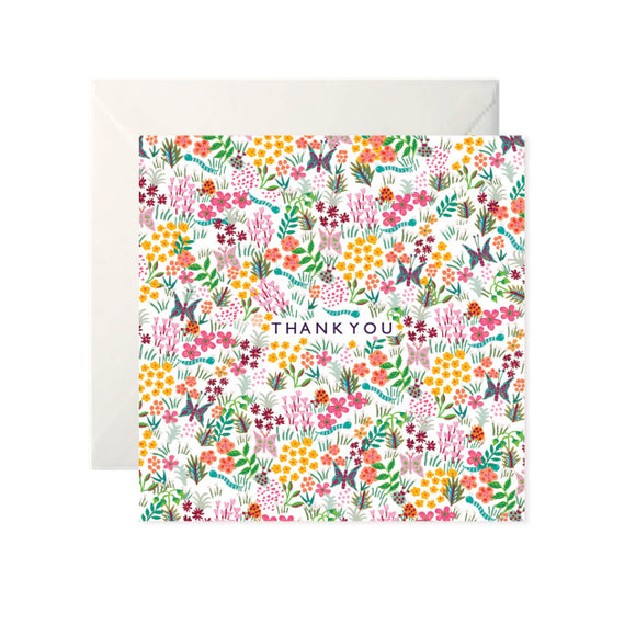 A white card with a drawn pattern of flowers and butterflies in bright colours. In the centre ‘Thank You’ is written in black capitals.