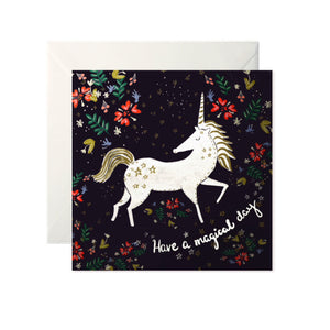 A black card with a painted floral pattern. A white unicorn is in the centre with ‘Have a magical day’ written in white cursive underneath.