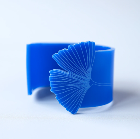 A blue cuff that is partially opened. One end is shaped like a ginkgo leaf with the designed etched into the bracelet.