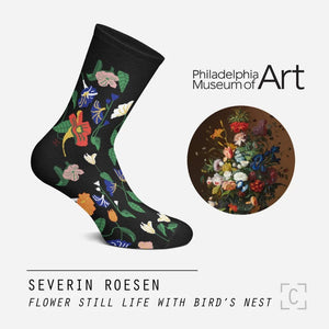 A black pair of socks with a pattern of colourful flowers across it. Beside is the realistic flower painting it’s based on.