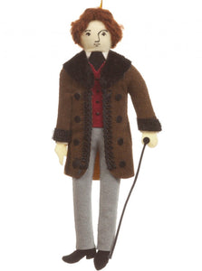 A felt man wearing a red waistcoat and long brown coat with a black trim, holding a walking stick, and hanging from a gold thread.