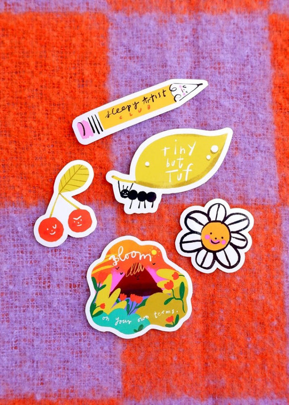 Five cartoon stickers: a smiling daisy, angry and winking cherries, a pencil, an ant carrying a leaf, a colourful landscape.