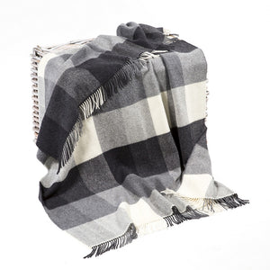A blanket coloured in blocks of white, grey and black, with a matching fringe across the top and bottom. There is a zigzag herringbone pattern across the blanket.